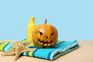 Halloween pumpkin with starfish, sunscreen cream and towel on blue background