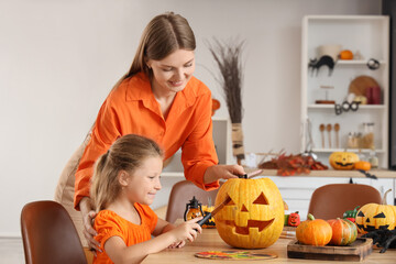 Little girl with her mother carving Halloween pumpkin at table in kitchen