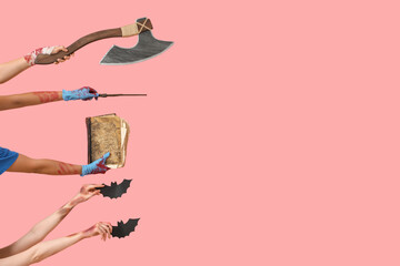 Hands of zombies with axe, old book, magic wand and bats on pink background. Halloween celebration