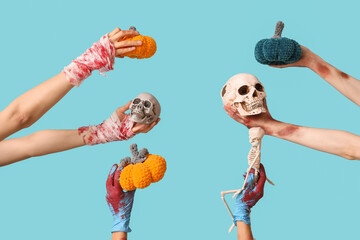 Hands of zombies with knitted pumpkins, skeleton and human skulls on color background. Halloween...