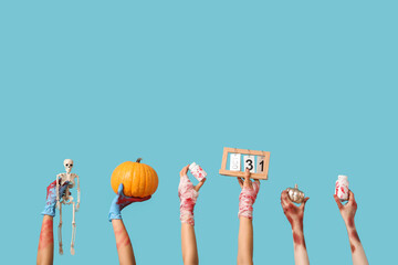 Hands of zombies with decorations, pumpkin and calendar for Halloween on color background