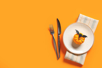 Beautiful table setting with fresh pumpkin and paper bat for Halloween celebration on orange...
