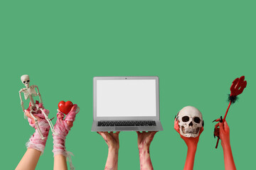 Mummy, zombie and devil hands with laptop and Halloween decorations on green background