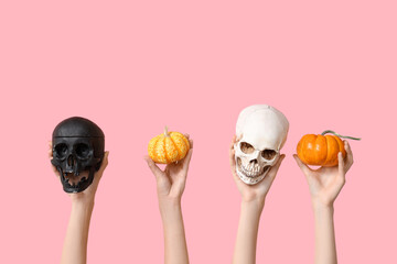 Female hands with skulls and pumpkins on pink background. Halloween celebration
