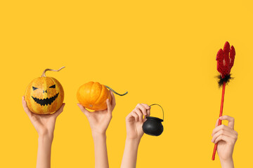Female hands with pumpkins, pitchfork and pot on yellow background. Halloween celebration