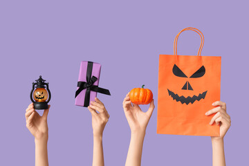 Female hands with lantern, gift box, pumpkin and shopping bag on lilac background. Halloween...
