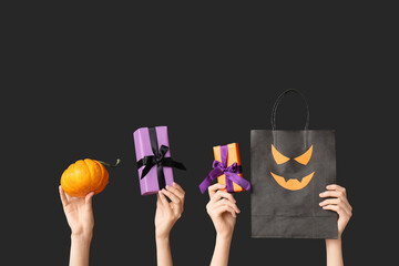 Female hands with pumpkin, gift boxes and shopping bag on black background. Halloween celebration