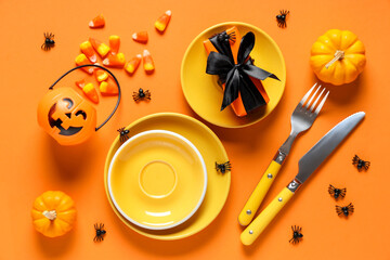 Festive table setting for Halloween celebration with gift box, candies and pumpkins on orange...