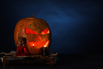 Halloween composition with jack-o-lantern, spell book and bottle of poison on table near blue wall