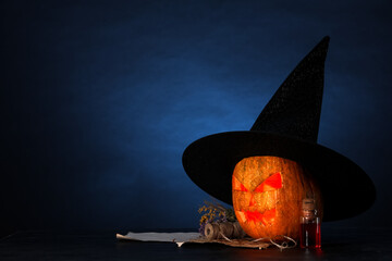 Halloween composition with jack-o-lantern in witch hat, flowers and bottle of poison on table near...