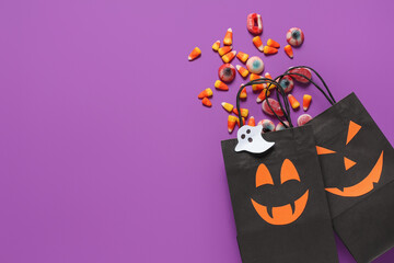 Halloween shopping bags with different candies on purple background