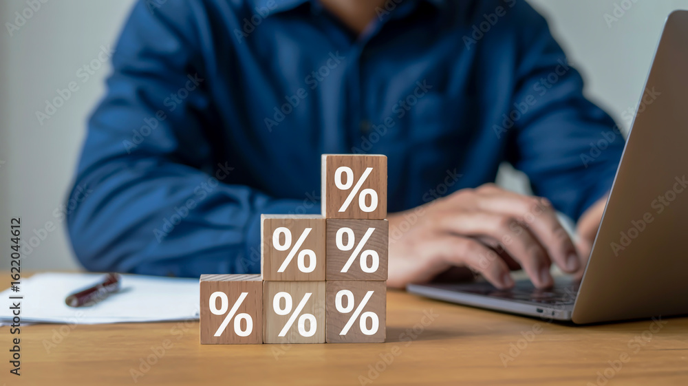 Poster wooden blocks with percentage symbols stacked in a pyramid shape with a person typing on a laptop in