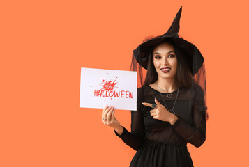Young happy Asian woman dressed as witch pointing at text HALLOWEEN SALE on orange background