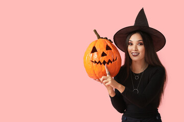Young happy Asian woman dressed as witch for Halloween with carved pumpkin showing silent gesture...