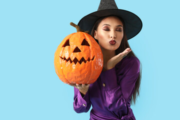 Beautiful young happy Asian woman dressed as witch for Halloween with carved pumpkin blowing kiss...