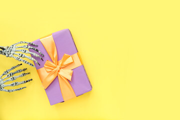 Halloween gift and hands of skeleton on yellow background. Top view