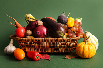Wicker basket with fresh vegetables, fruits and autumn leaves on green background. Harvest festival