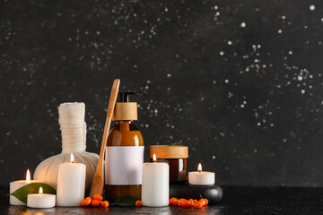 Composition with natural cosmetic products, herbal massage bag, burning candles and sea buckthorn on dark background