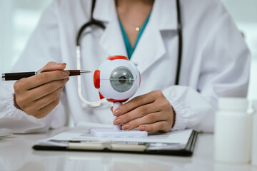 An Asian ophthalmologist examines an elderly patient's eyes for conditions like cataracts,...
