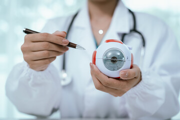 An Asian ophthalmologist examines an elderly patient's eyes for conditions like cataracts,...