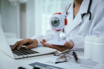An Asian ophthalmologist examines an elderly patient's eyes for conditions like cataracts,...