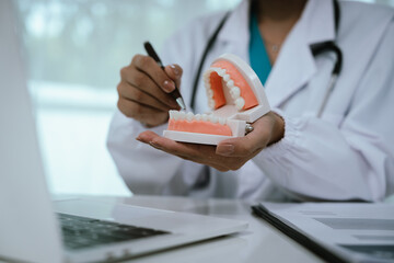 A dentist explains oral health using a dental model, demonstrating proper teeth alignment and hygiene during a patient consultation at a modern dental clinic or hospital.
