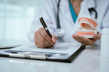 A dentist explains oral health using a dental model, demonstrating proper teeth alignment and hygiene during a patient consultation at a modern dental clinic or hospital.