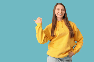 Happy young beautiful woman pointing at something on blue background