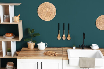 Interior of light kitchen with shelving unit and white counters near blue wall