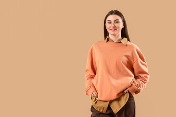 Stylish young woman in eyeglasses on beige background