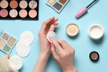 Young woman removing lipstick from hand and makeup products on blue background