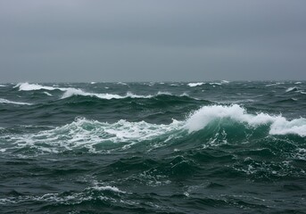 Fototapeta premium Powerful ocean waves crash dramatically against the rugged coastal rocks, creating a foamy blue splash under the summer sky