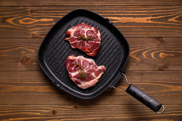 Frying pan with fresh raw steaks and thyme on wooden background