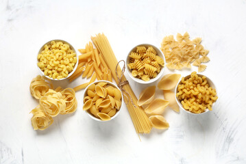 Bowls with different types of raw pasta on white background