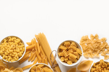 Bowls with different types of raw pasta on white background