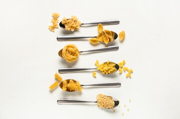 Spoons with different types of raw pasta on white background