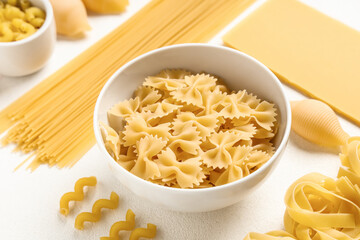 Bowl with different types of raw pasta on white background, closeup