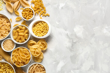 Bowls with different types of raw pasta on grey grunge background