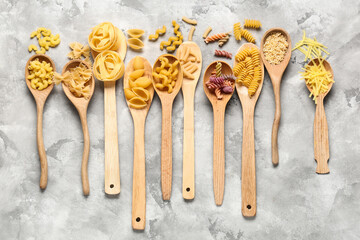 Wooden spoons with different types of pasta on grey grunge background
