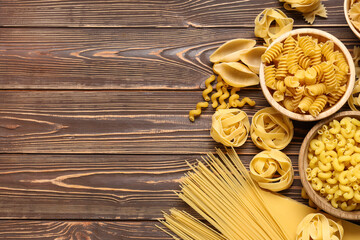 Bowls with different types of pasta on wooden background