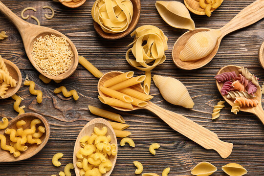 Wooden spoons with different types of pasta on wooden background