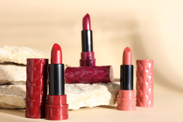 Beautiful lipsticks and decorative stones on beige background, closeup
