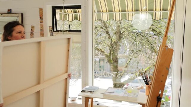 Painter puts canvas on easle in scenic studio, side view
