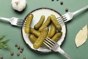 Plate with tasty pickled cucumbers and different spices on green background