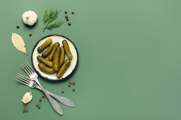 Plate with tasty pickled cucumbers and different spices on green background
