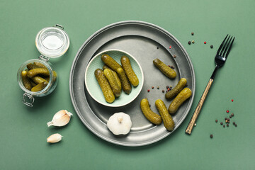 Bowl with tasty pickled cucumbers, garlic and peppercorns on green background