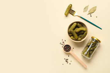 Bowl and jar with tasty pickled cucumbers on beige background