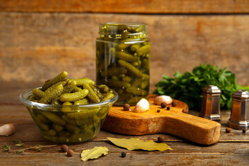 Glass bowl with tasty pickled cucumbers and different spices on wooden background
