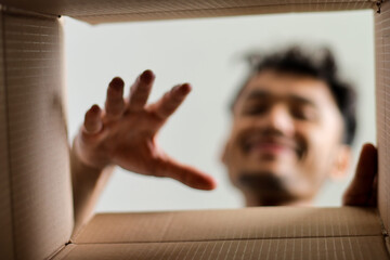Excited Young Man Reaching Into Open Box And Smiling As He Discovers A New Product