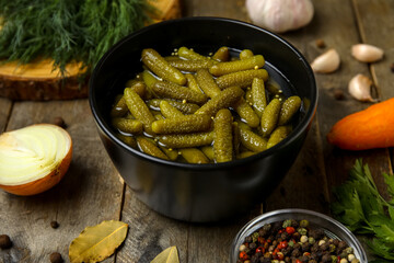 Bowl with tasty pickled cucumbers and different ingredients on wooden background, closeup